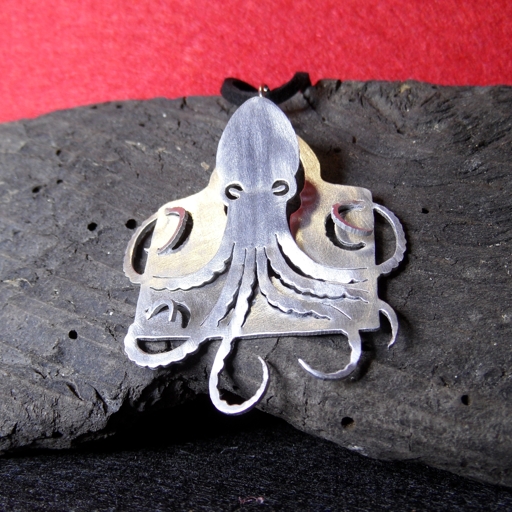 An aluminium pendant of an octopus, cut out of a metal frame and that looks like it is coming out of it