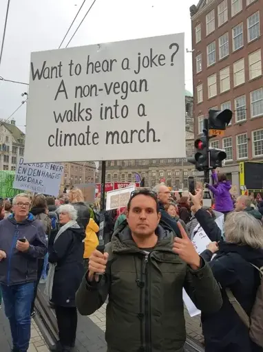 A man holding a board saying, "Want to hear a joke? A non-vegan walks into a climate march."