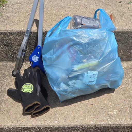 Blue plastic grocery bag full of garbage, a trash grabber and gloves on concrete steps